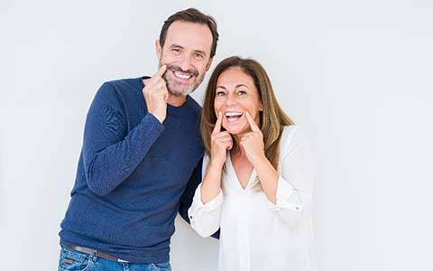 couple with dental implants in Corte Madera pointing to their smiles