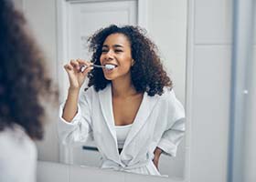 woman in a white bathrobe brushing her teeth