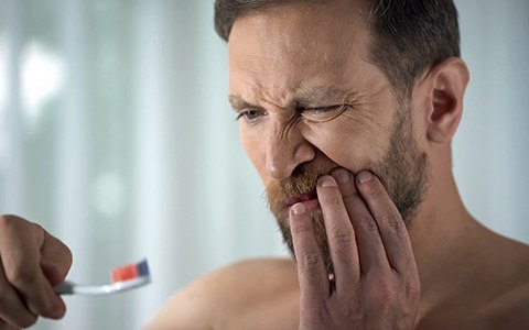 Man frowning at his toothbrush, concerned about bleeding gums