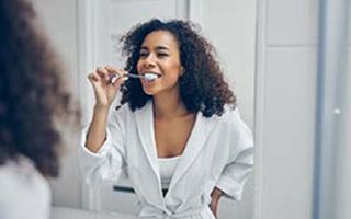 woman in a white bathrobe brushing her teeth