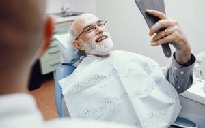 Man smiling in dental chair with handheld mirror